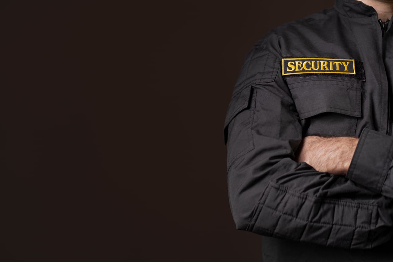 Security operative in black uniform with arms crossed against dark background