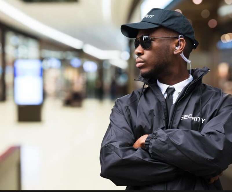 Male security operative in black jacket with sunglasses and earpiece, arms crossed
